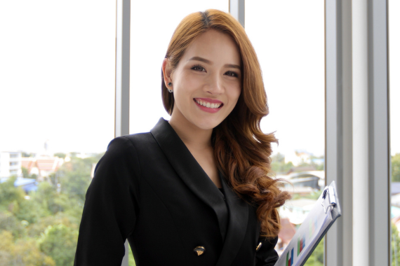 smiling woman in black suit holding a folder in front of a window